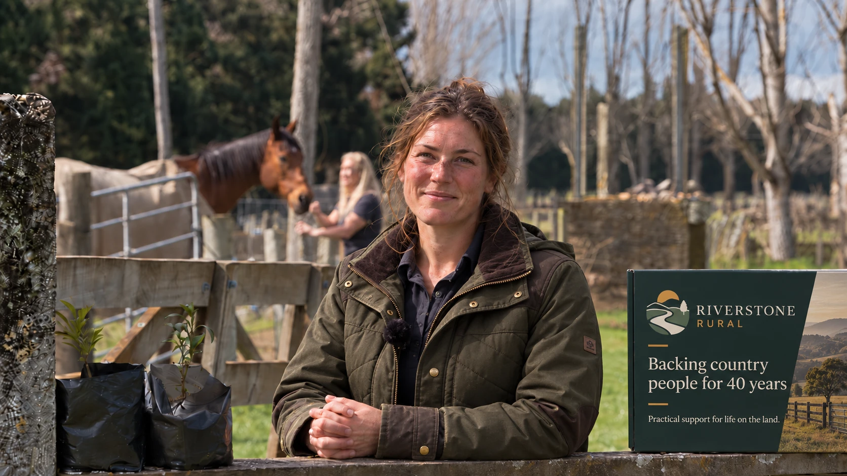 A smiling farmer in a waxed jacket leans on a gate beside a branded gift box, with a horse and paddocks behind her.